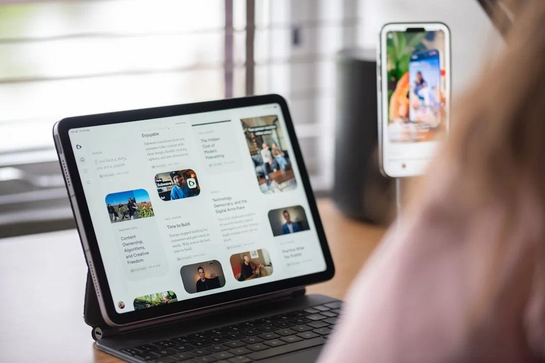 Des mains tiennent une tablette à côté d’un ordinateur portable dans un bureau à domicile, illustrant la navigation en ligne.